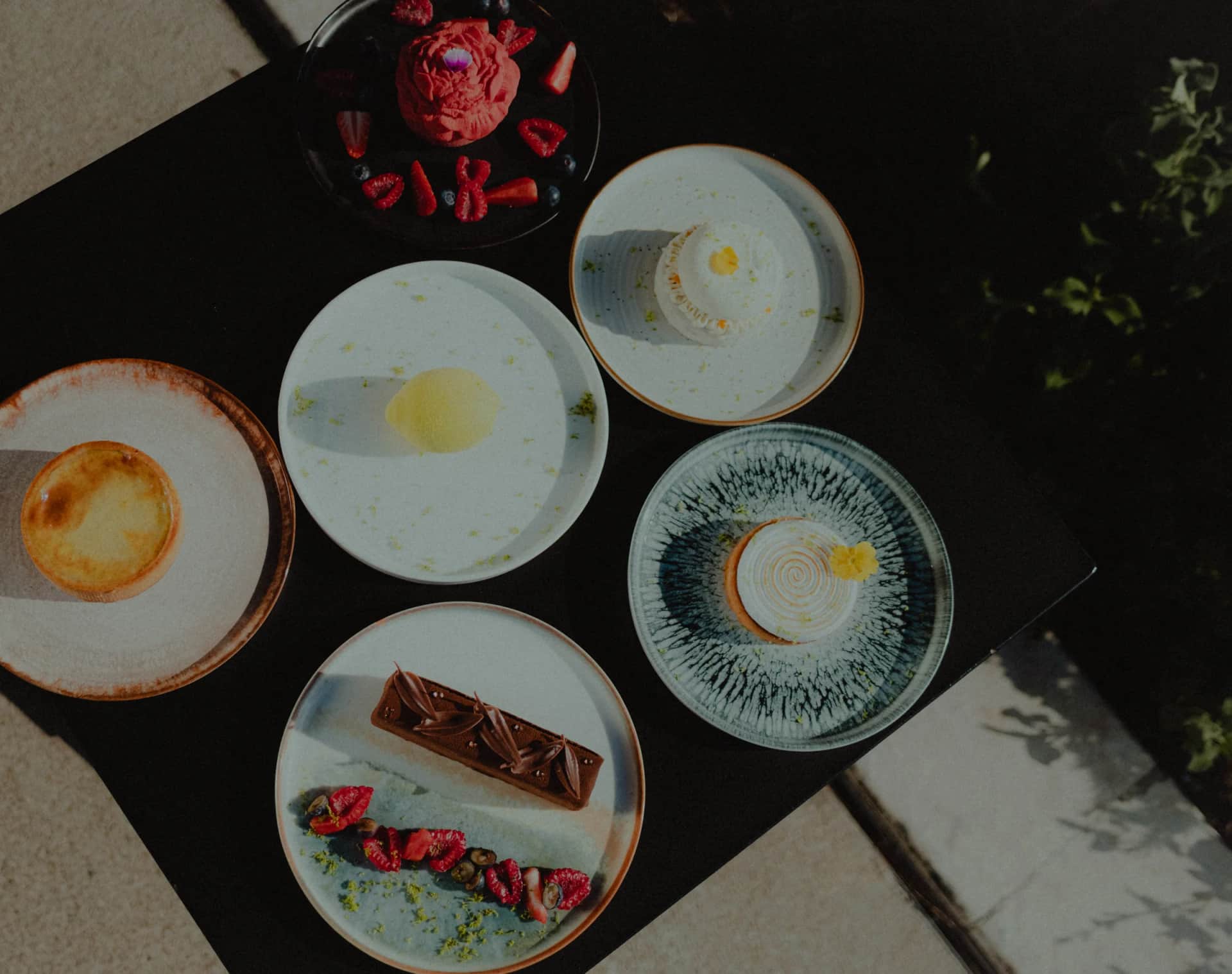 Six desserts du chef pâtissier dressés sur une table en terrasse, vus de dessus